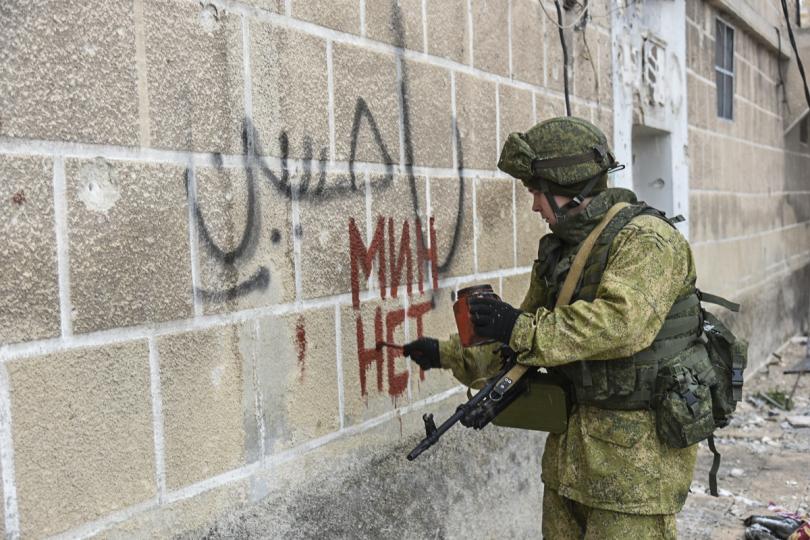 A soldier daubs graffiti written in Russian on a wall in Aleppo, underneath previous graffiti written in Arabic