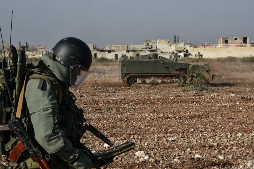 A Russian soldier studies his equipment as an army vehicle drives past him