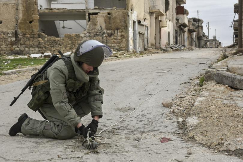 A heavily armed Russian soldier works on the ground in the deserted streets of the Syrian city