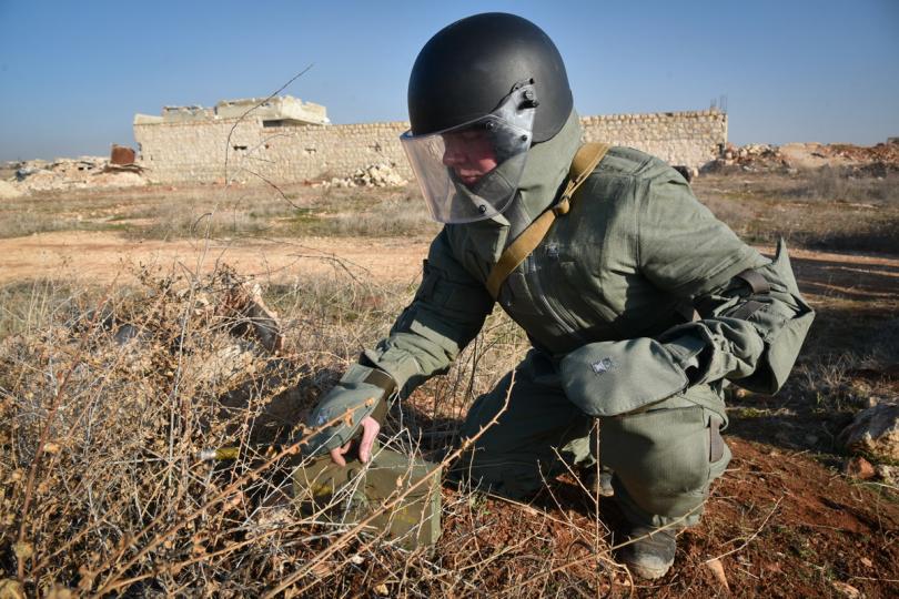 A member of Russian military personnel checks his equipment, behind the thorny Syrian ground